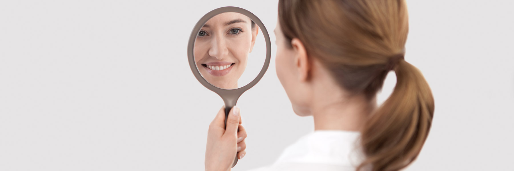Frau mit schönen Zähnen betrachtet sich im Spiegel
